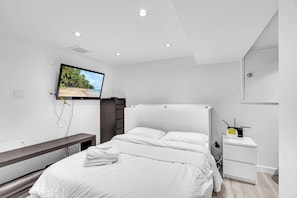 A modern bedroom with a bed, a TV mounted on the wall, a bedside table, and a desk with a computer. - Modern & Minimalist 2-Bed Suite Near UBC (Vancouver)