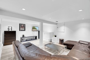 Una sala moderna con un sofá de cuero marrón, una mesa de centro de vidrio y un mueble de entretenimiento blanco.