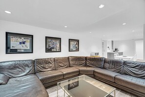 A modern living room with a leather sectional sofa, a glass coffee table, and framed sports memorabilia on the wall. - Modern & Minimalist 2-Bed Suite Near UBC (Vancouver)