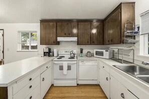 A modern kitchen with white appliances, wooden cabinets, and a stainless steel sink. - Cozy 3BR Broadview Retreat | Near Transit & Parks (Seattle)