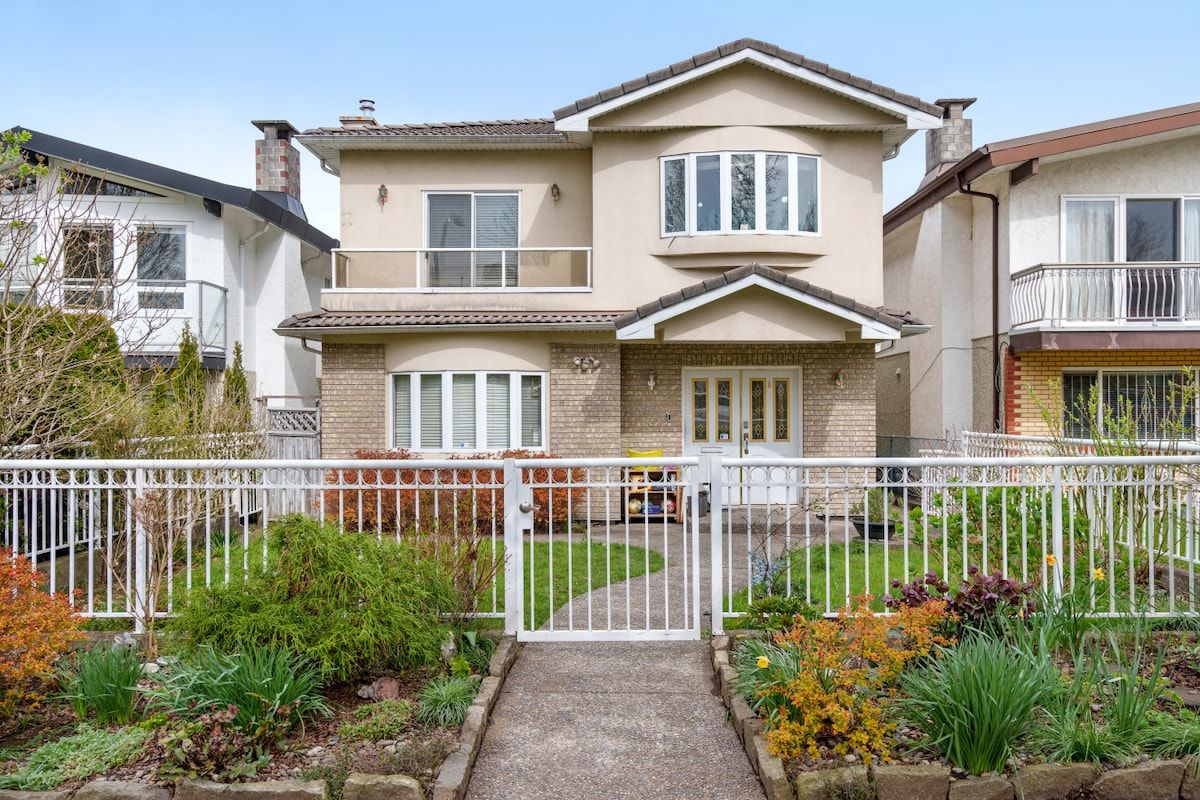 A two-story house with a front porch, a gated driveway, and a well-maintained garden.