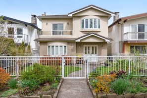 A two-story house with a front porch, a gated driveway, and a well-maintained garden. - Bright & Comfy 1BR Suite | Vancouver’s Prime Area (Vancouver)