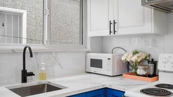 A kitchen with white cabinets, a black faucet, a white microwave, and a stove.