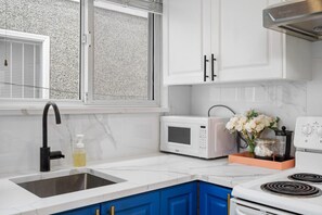 A kitchen with white cabinets, a black faucet, a white microwave, and a stove. - Bright & Comfy 1BR Suite | Vancouver’s Prime Area (Vancouver)