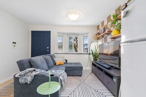 A modern living room with a grey sectional sofa, a flat-screen TV, and a patterned rug. - Bright & Comfy 1BR Suite | Vancouver’s Prime Area (Vancouver)