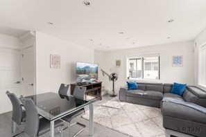 A modern living room with a glass dining table, grey sofas, and a large window. - Sleek Coach House - Designer Kitchen - Sleeps 7 (Vancouver)