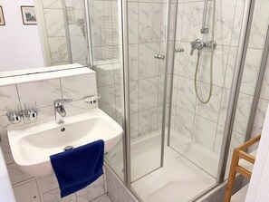 A bathroom with a glass-enclosed shower, a white sink with a blue towel, and marble tiles. - Holiday Apartments With Baltic Sea View (Heringsdorf)