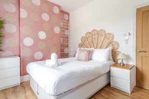 A bedroom with a bed, a nightstand, a wooden door, and a wall with a circular pattern. - Cardiff Bay Victorian House Garden Sleeps 5 (Cardiff)