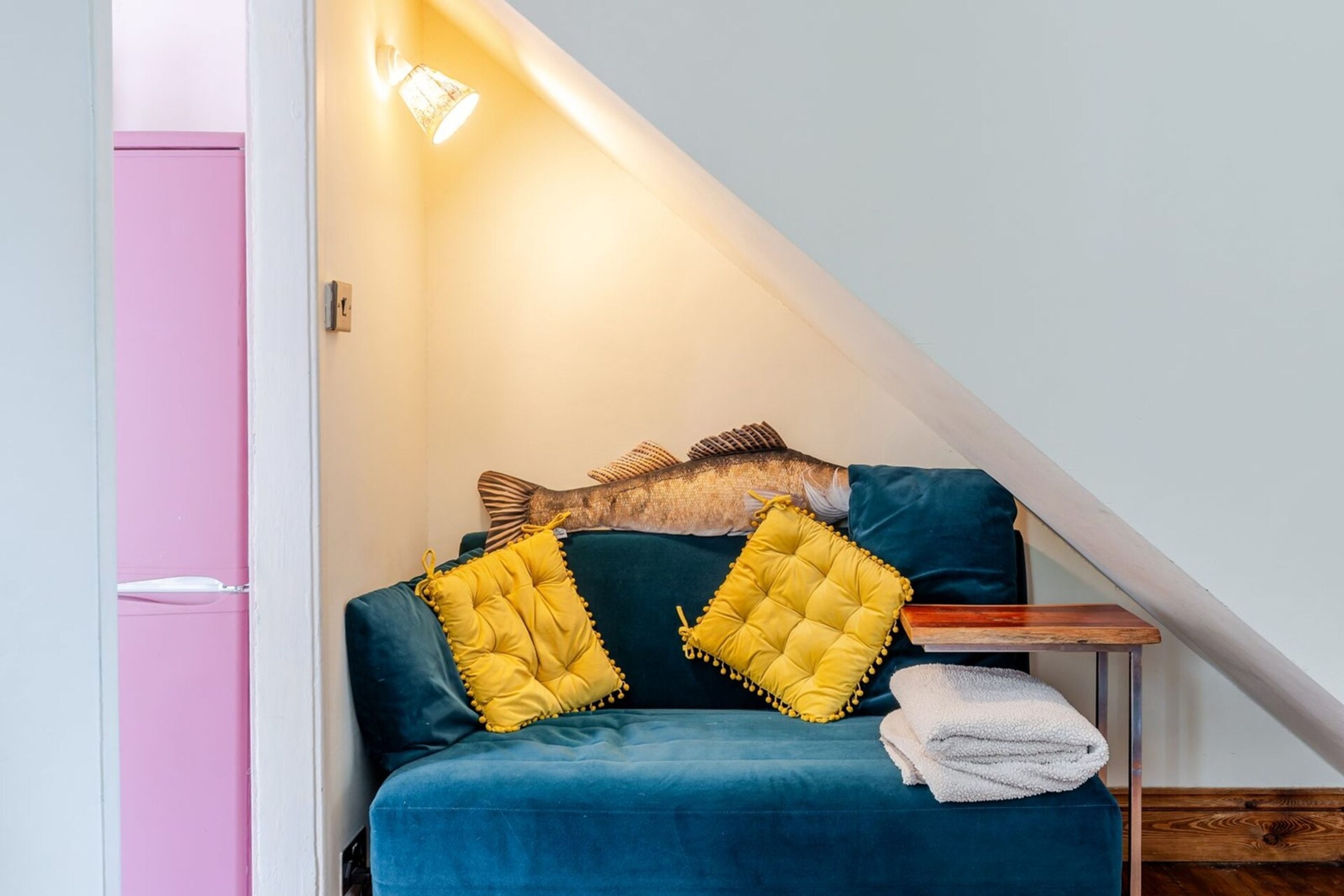 A cozy room with a blue sofa, two yellow pillows, a wooden side table, and a white towel.