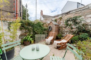 A patio with a round table, two wooden chairs, a small wooden structure, and potted plants. - Cardiff Bay Victorian House Garden Sleeps 5 (Cardiff)