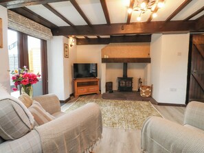 A cozy living room with a fireplace, wooden beams, a television, and comfortable seating. - The Thatched Cottage (Preston)