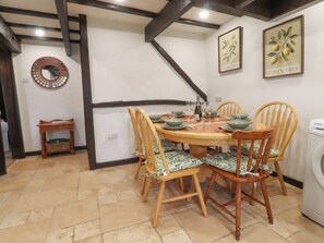 A dining area with a round table set for six, surrounded by wooden chairs with green cushions. - The Thatched Cottage (Preston)