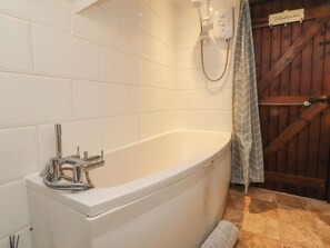 A bathroom with a white bathtub, a showerhead, and a wooden door with a sign. - The Thatched Cottage (Preston)