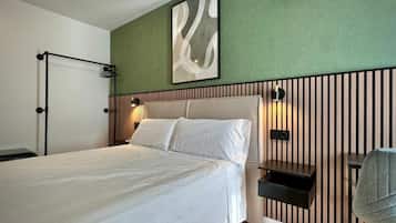 A hotel room with a bed, a wall-mounted air conditioner, a bedside table, and a chair.