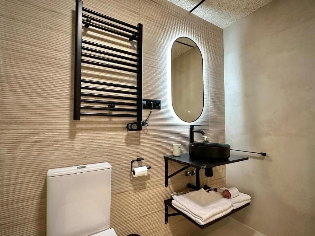 A modern bathroom with a towel rack, a mirror, a sink with a black basin, and a toilet.