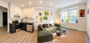 A modern kitchen with a built-in oven and dishwasher, a green sofa, and a small side table with a plant. - Big 2 rooms appartement 5mn from metro cote ste catherine / pet friendly (Montréal)