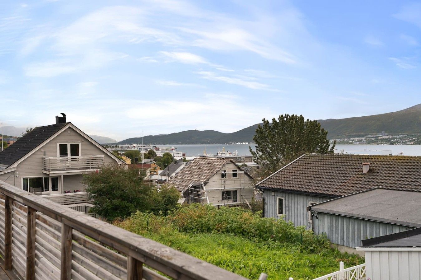 Un quartier résidentiel avec des maisons, une clôture en bois et une vue sur la mer et les collines.