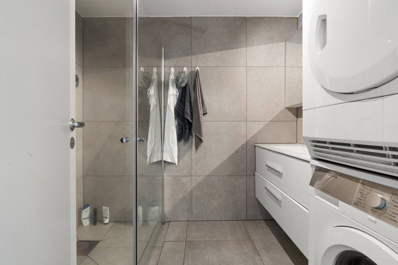 Een moderne badkamer met een glazen douchecabine, een ingebouwde wasmachine en een handdoekrek met meerdere handdoeken.