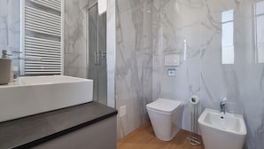 A modern bathroom with a marble wall, a bathtub, a toilet, and a sink. - Italianway Comfort - Tunisia 22 (Milan)