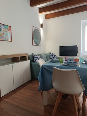 Ein Essbereich mit einem Tisch für zwei Personen, einer Couch und einem Fernseher.