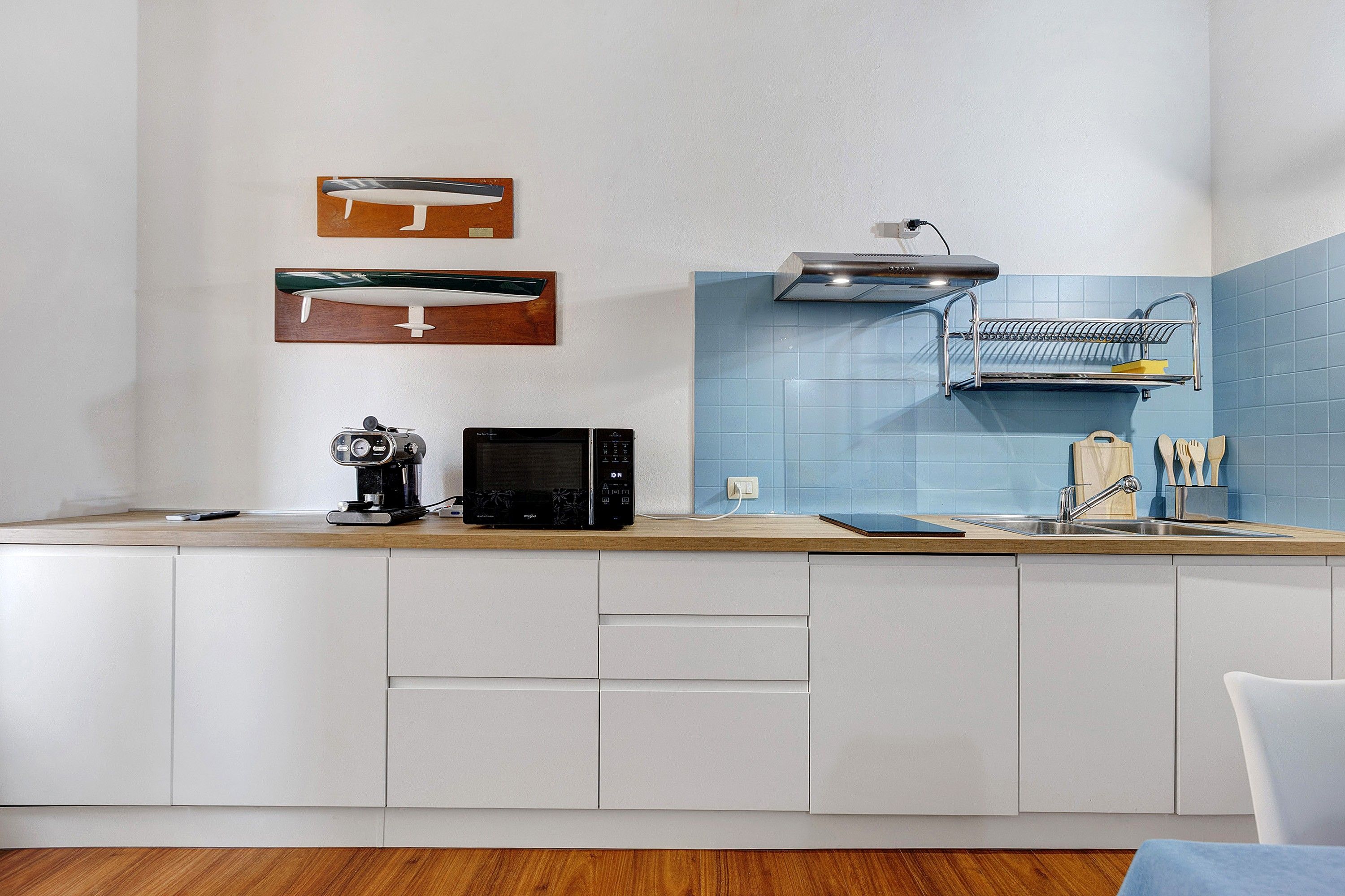 A modern kitchen with white cabinets, a microwave, a coffee maker, and a sink with a dish rack above it.