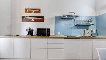 A modern kitchen with white cabinets, a microwave, a coffee maker, and a sink with a dish rack above it.
