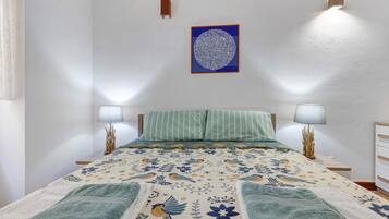 A bedroom with a bed, two bedside lamps, a wall-mounted light fixture, and a framed artwork.