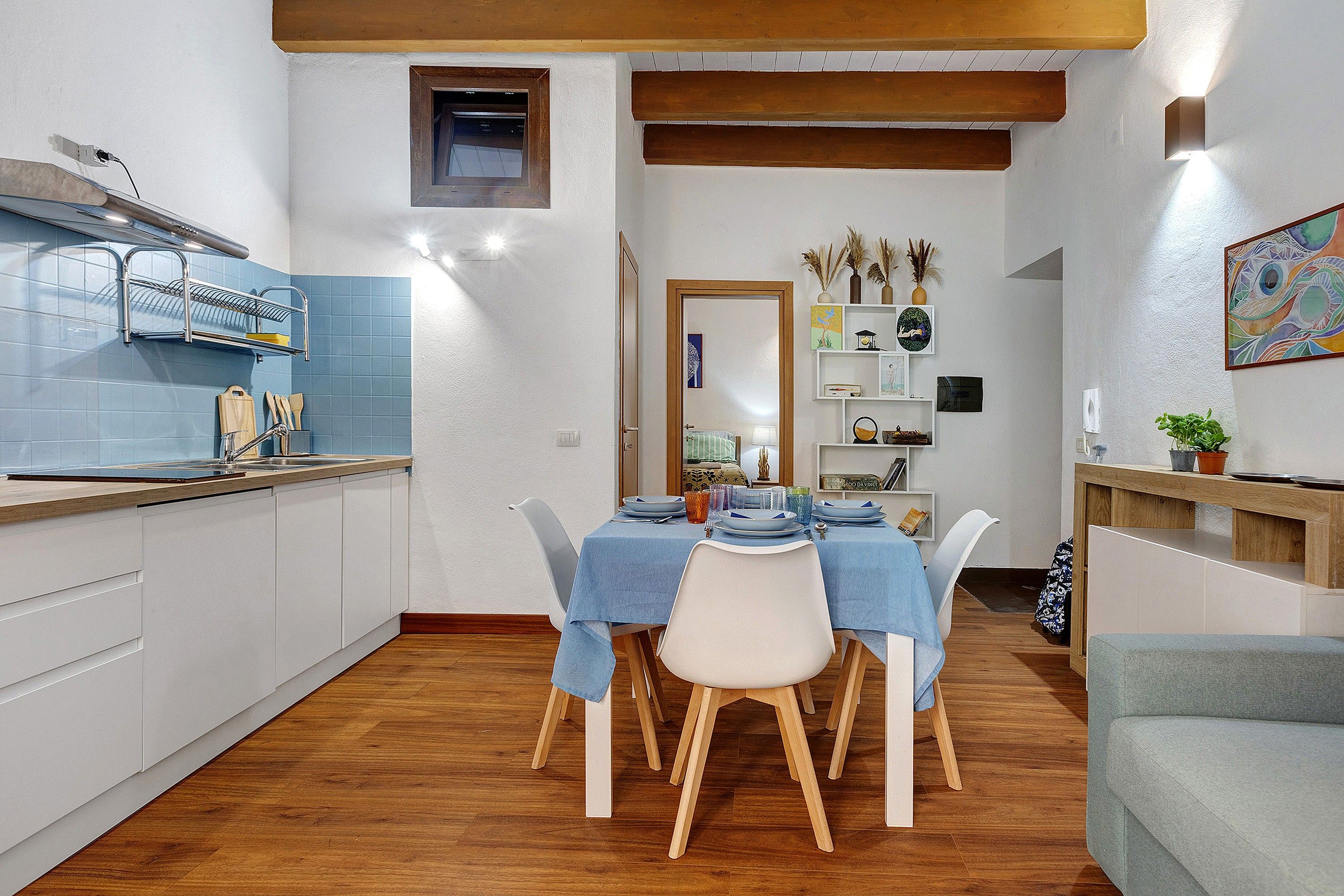 A compact kitchen with a dining area, wooden flooring, and a small window.