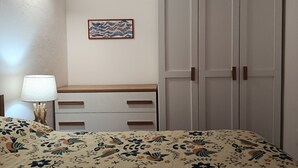 Ett sovrum med en säng, en byrå, en garderob, en vägglampa och en inramad tavla.