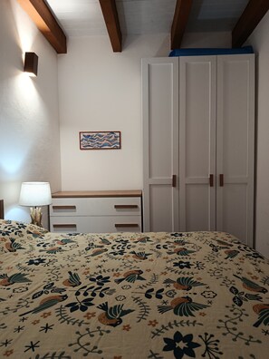 Ein Schlafzimmer mit einem Bett, einem Schminktisch, einem Kleiderschrank, einer Wandlampe und einem gerahmten Bild.