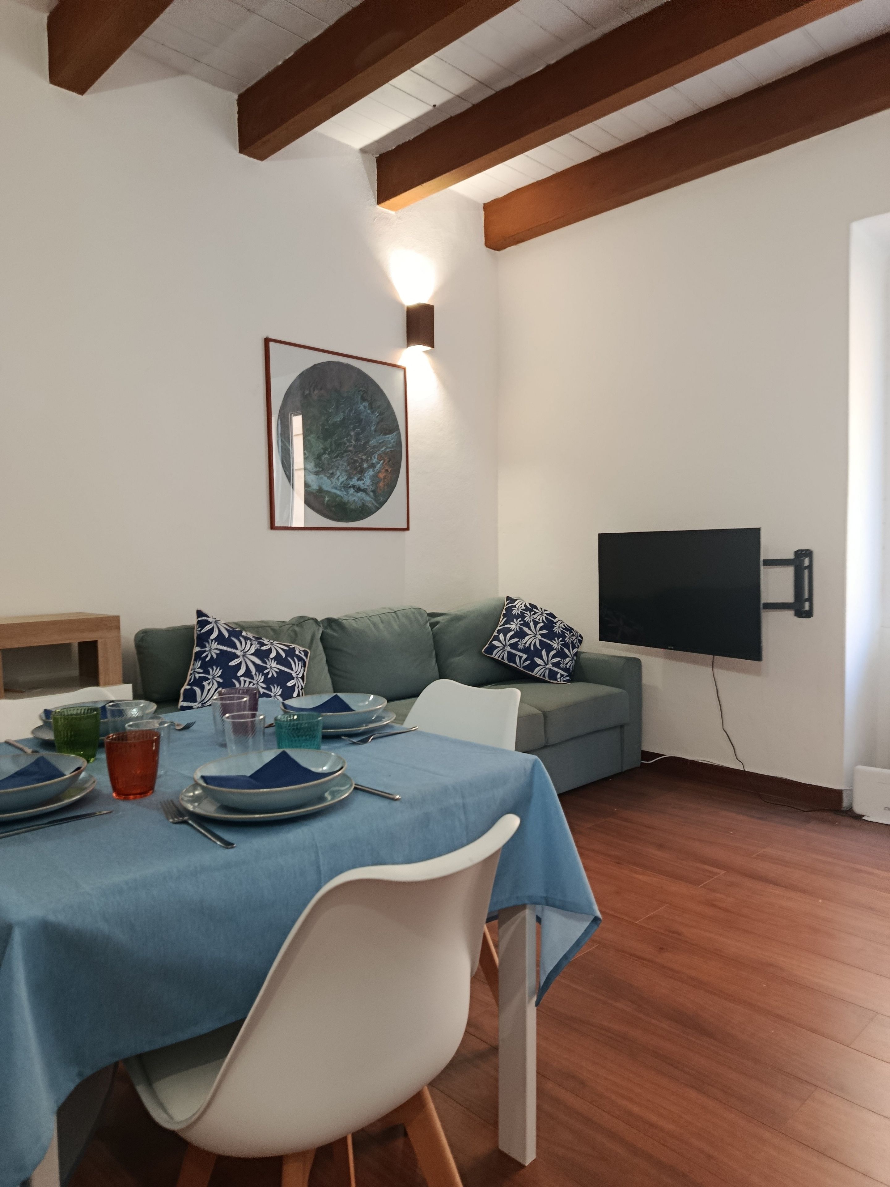 Een eetgedeelte met een tafel gedekt voor twee personen, een bank met gestreepte kussens, een wandgemonteerde flatscreen-tv en een kunstwerk in een lijst aan de muur.