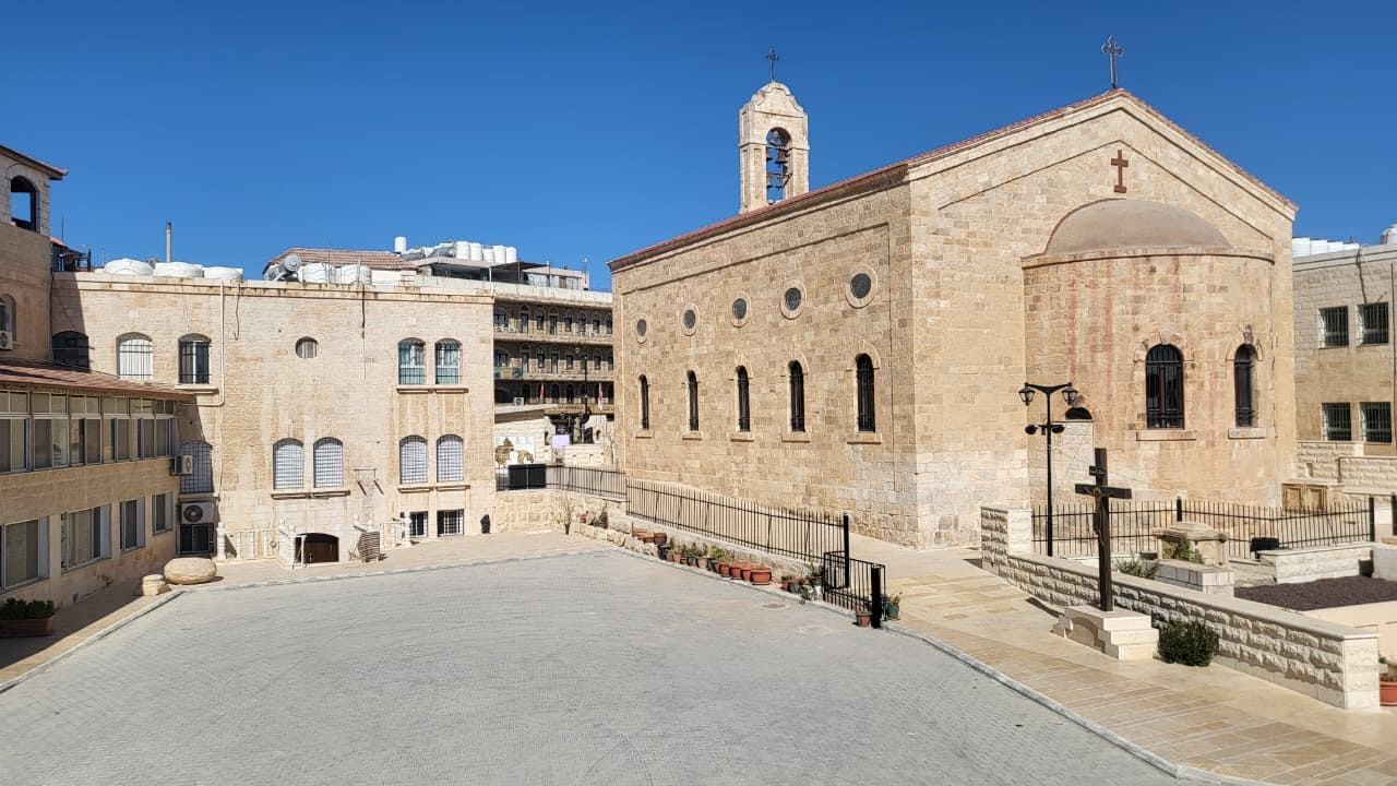 A courtyard with a large open space, a building with a dome and arched windows, and a bell tower.