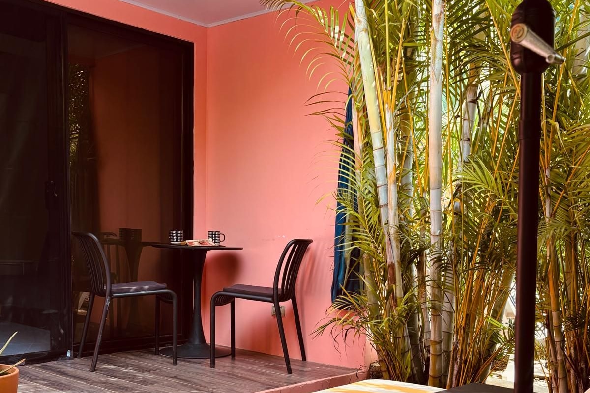 A sunlit outdoor seating area with striped lounge chairs, a table, and chairs, surrounded by tropical plants and a bamboo structure.