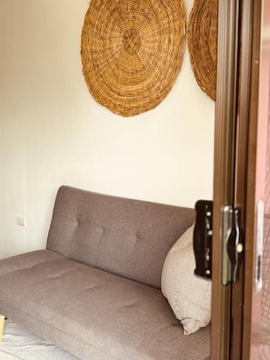 A room with a sofa, a door with a handle, and two woven wall hangings.