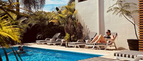 Una piscina con sillas de descanso, rodeada de palmeras y un edificio blanco.