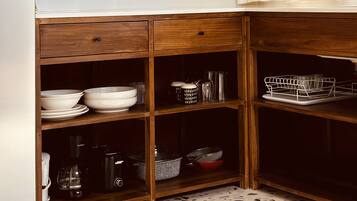 Una cocina con lavavajillas integrado, un televisor de pantalla plana montado sobre la encimera y un armario de madera con estantes abiertos que contienen utensilios de cocina.