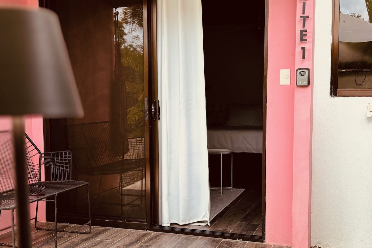 A room with a sliding glass door leading to an outdoor area, a chair, a table with a cup and saucer, and a sign reading 'SUITE 1'.
