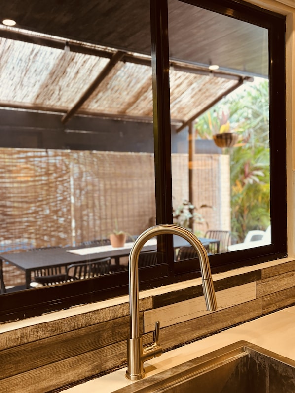 A kitchen with a stainless steel sink, a window overlooking an outdoor dining area with a table and chairs.