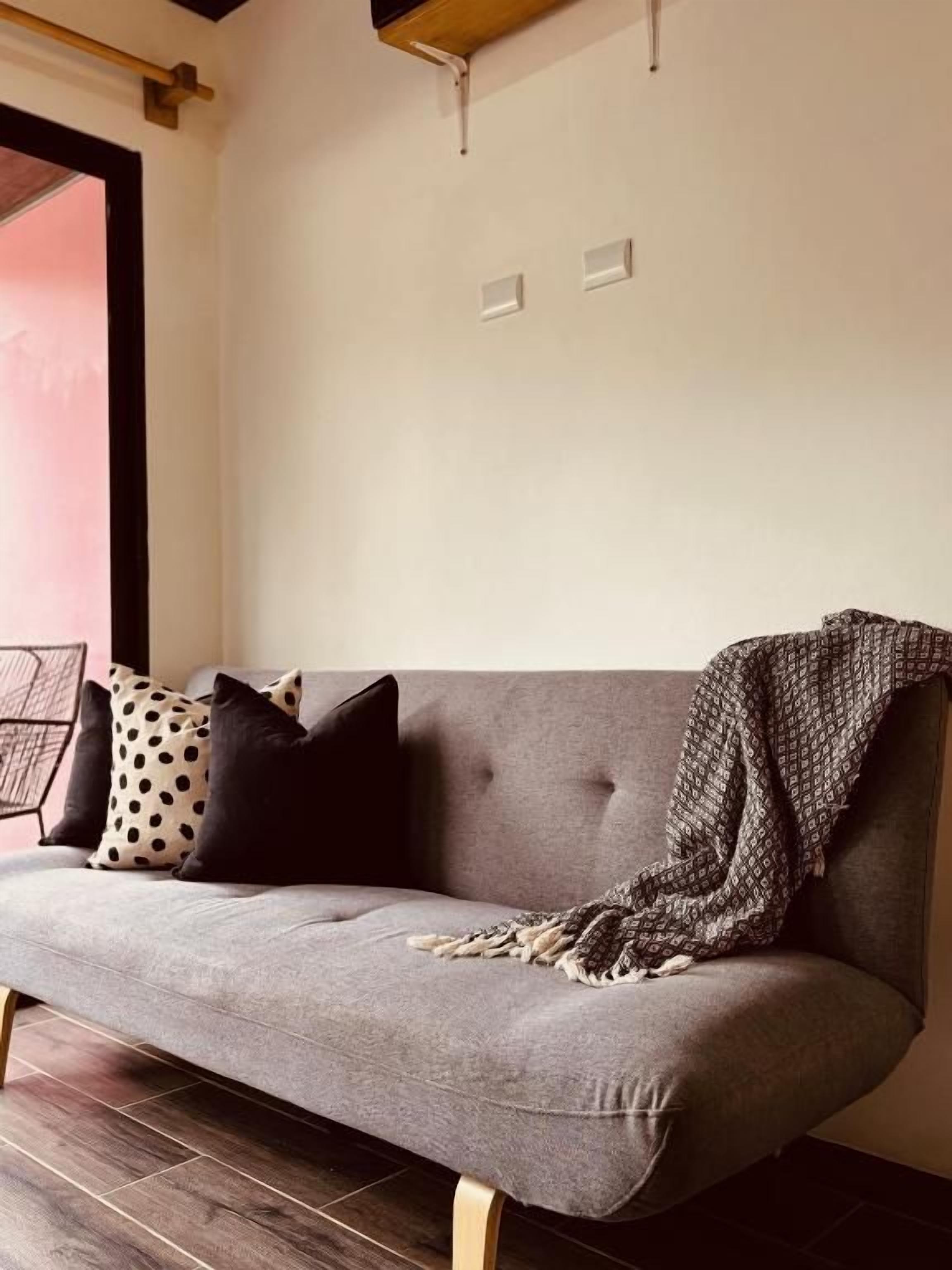 Um sofá cinzento com uma manta e almofadas estampadas, posicionado em frente a uma parede com dois interruptores de luz.