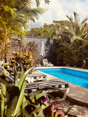 A pool area with lounge chairs and umbrellas, surrounded by lush greenery.