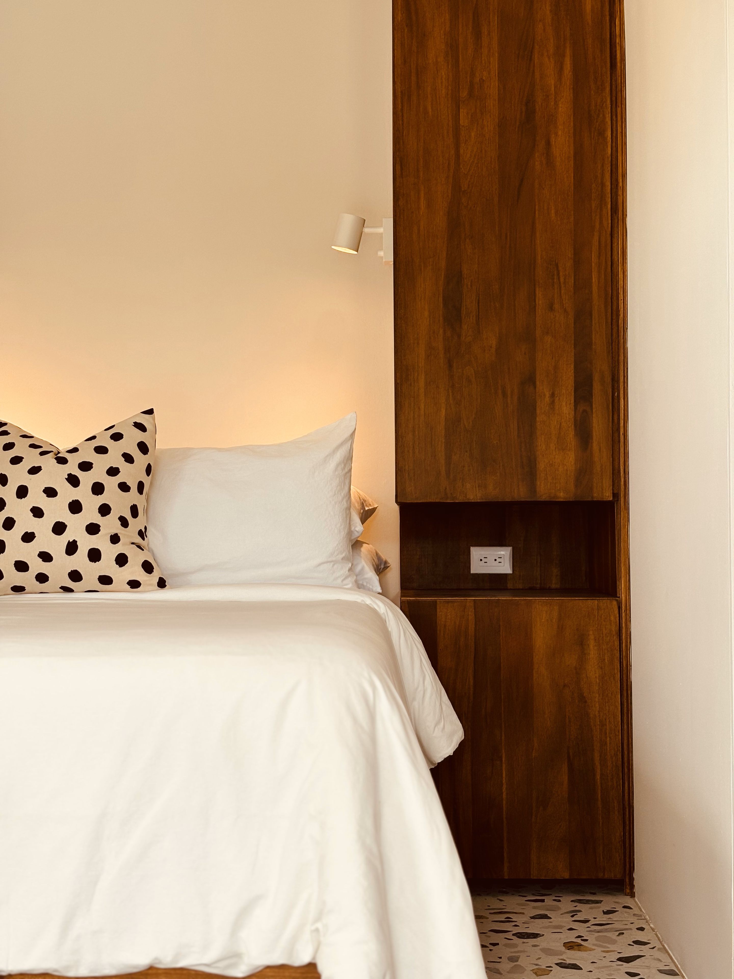 Un dormitorio con una cama, un armario de madera y una lámpara fijada a la pared.