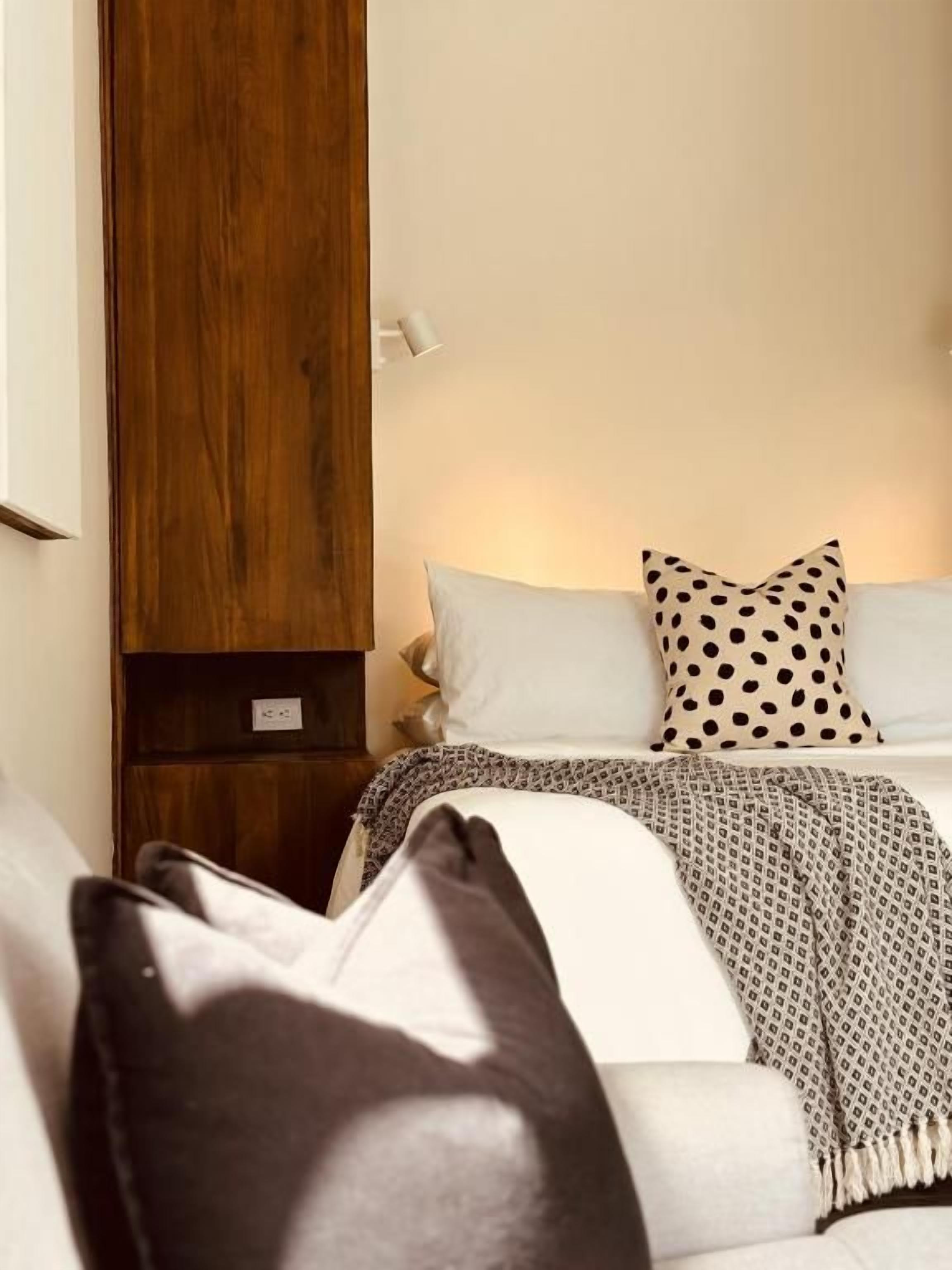 Un dormitorio con una cama, almohadas, una mesita de noche y un armario de madera.