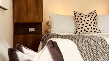 Un dormitorio con una cama, almohadas, una mesita de noche y un armario de madera.