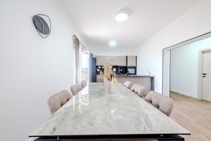 Une salle à manger moderne avec une table en marbre, six chaises et un vase contenant des plantes séchées.