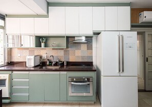 A kitchen with a built-in oven, a refrigerator, and a microwave. - SHB - 3 min praia - Central - Biquinha (São Vicente)