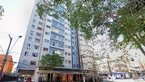 A multi-story building with a commercial ground floor, a parking area, and a tree-lined street.