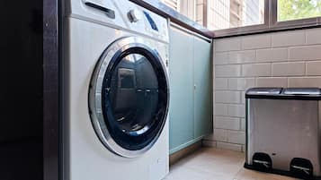 A compact, modern laundry room with a front-loading washing machine, a trash bin, and a window providing natural light.