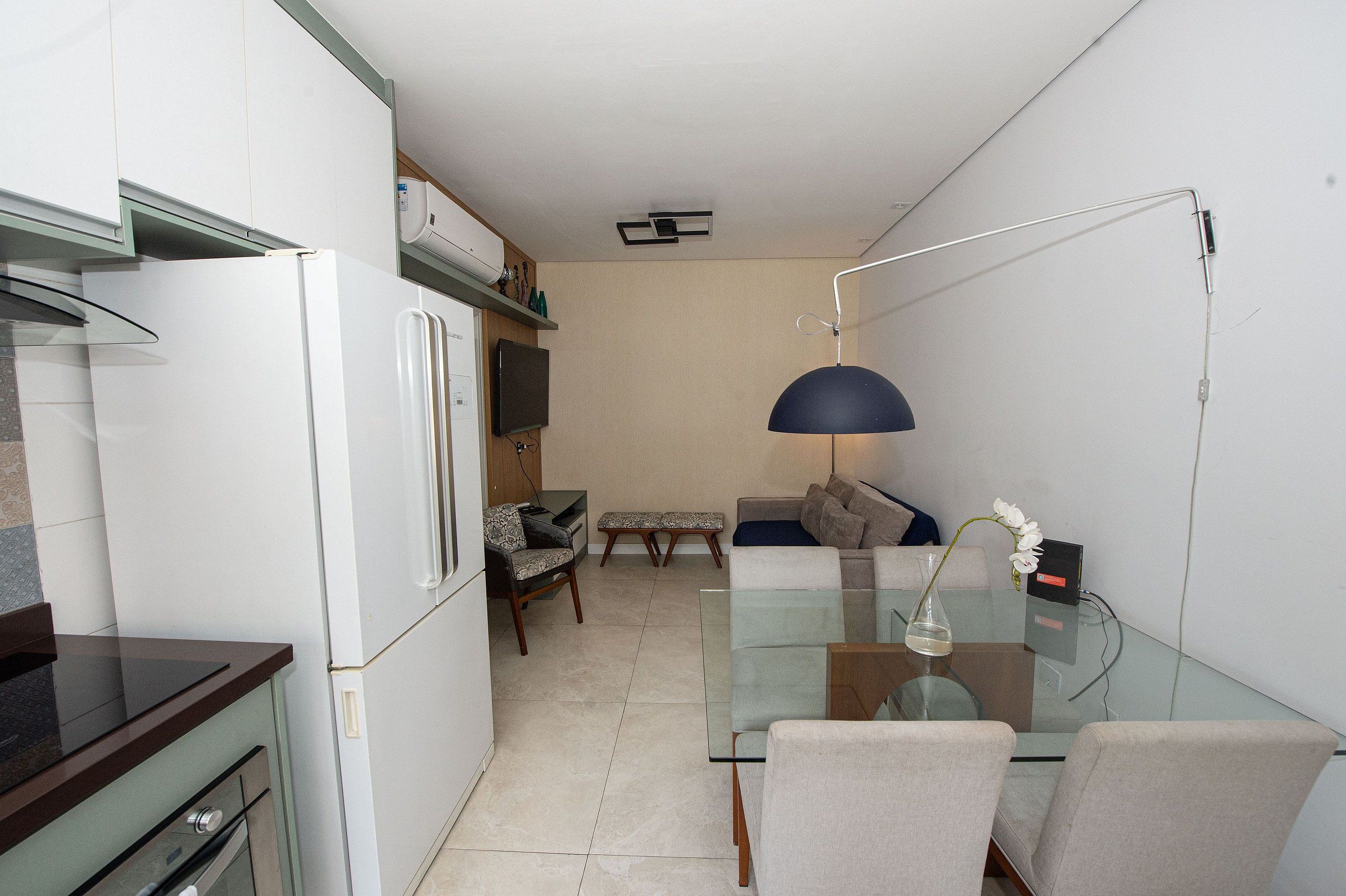 Una cocina compacta con refrigerador, microondas y una mesa de vidrio con sillas.