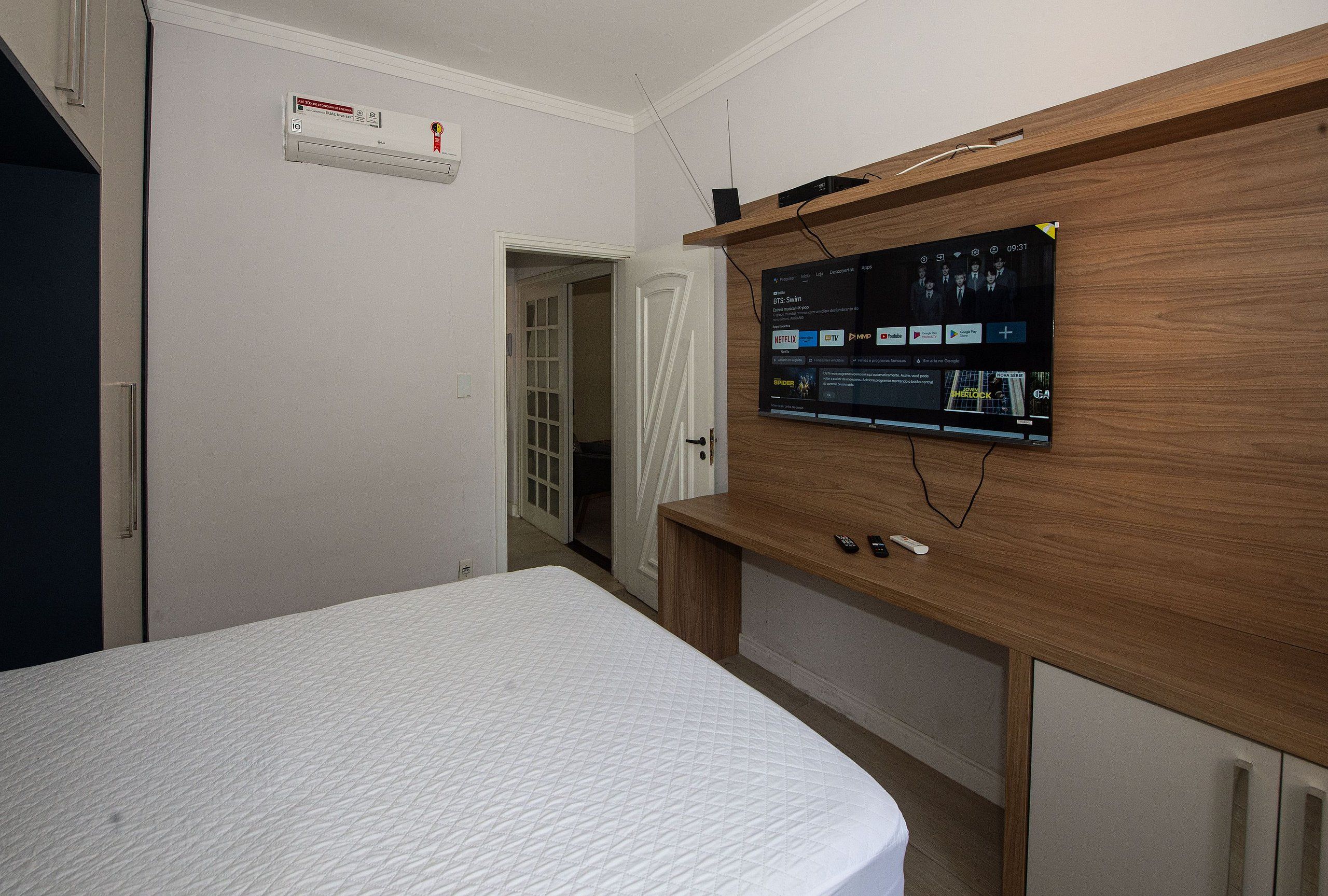 Un dormitorio con una cama, un televisor montado en un mueble de madera y un aire acondicionado blanco en la pared.