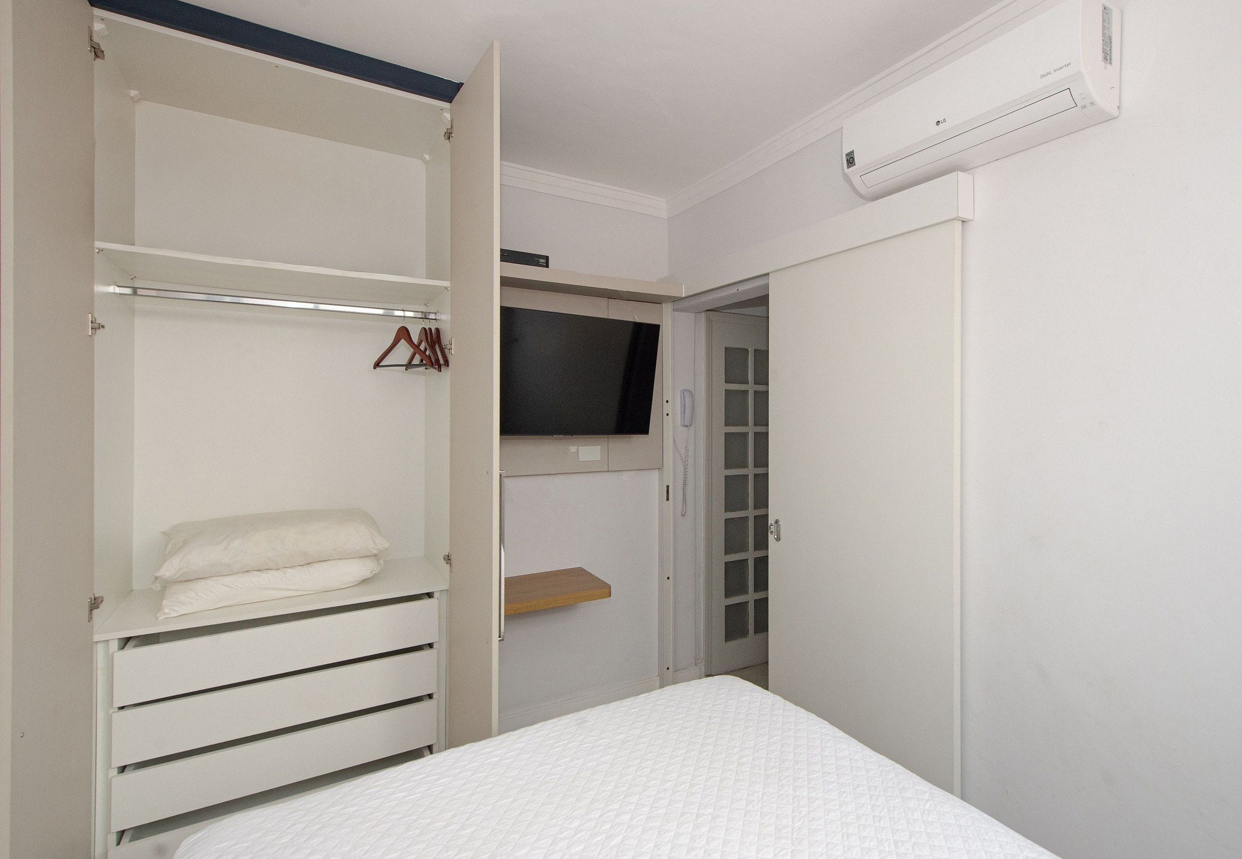 A bedroom with a bed, a wardrobe, a television, and a door leading to another room.